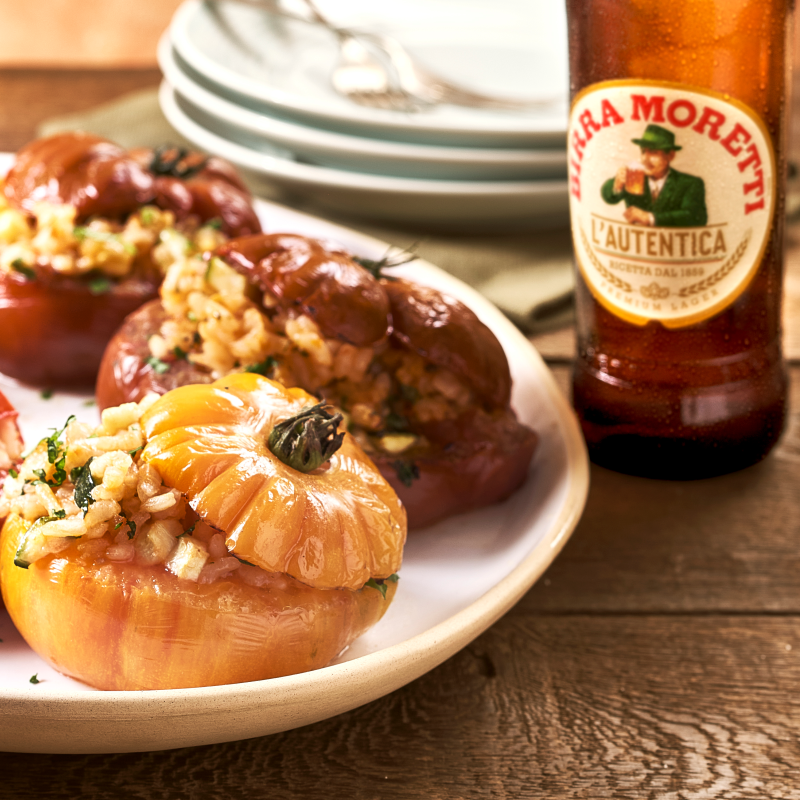 Stuffed tomatoes on a plate next to a bottle of Birra Moretti.