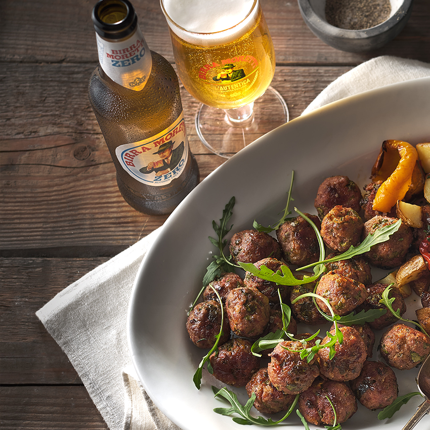 Meatballs garnished with arugula, served on a plate alongside Birra Moretti Zero.
